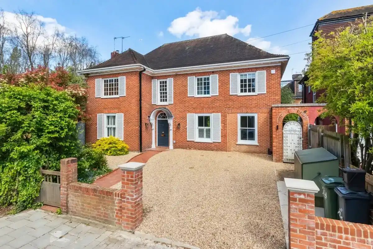 Front of a red-brick detached house with white shutters and a gravel drive