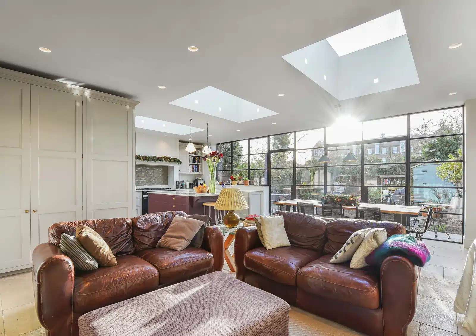 Open-plan kitchen, dining and sitting space in a Wimbledon rear extension, with rooflights and black steel-framed glazing to the garden.