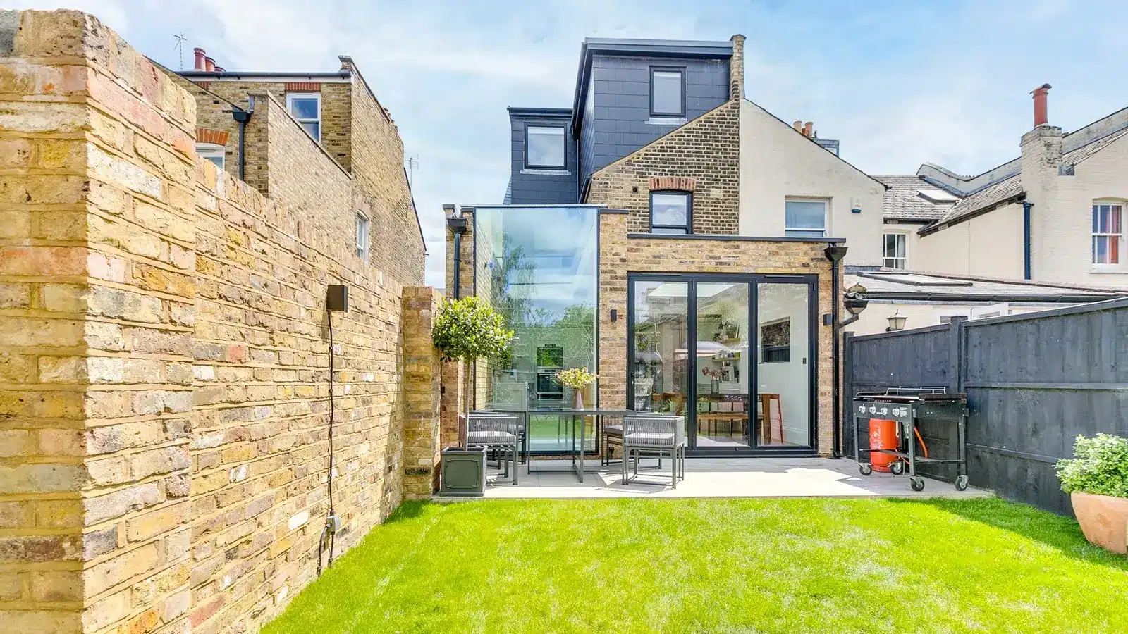 Rear of a Victorian end terrace with a glass side infill and a rear extension with sliding doors, seen from the garden, Earlsfield SW17