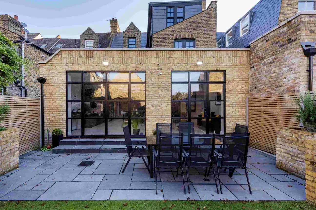 Rear of a Victorian house with a stock brick extension and black steel doors opening to a patio, Balham SW17