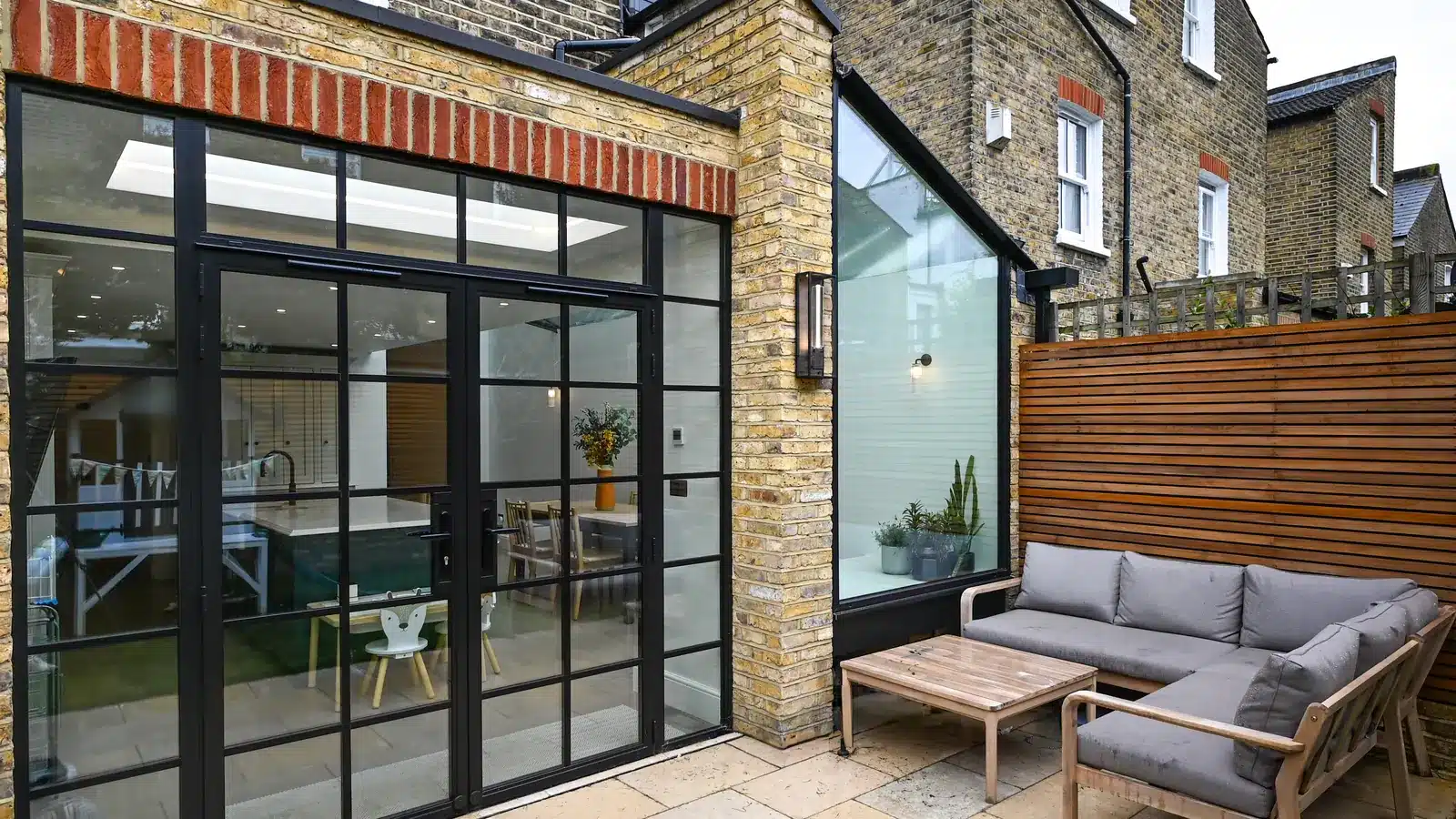Single-storey rear extension in yellow stock brick with Crittall-style doors and a glazed side bay, seen from the patio, Putney SW15